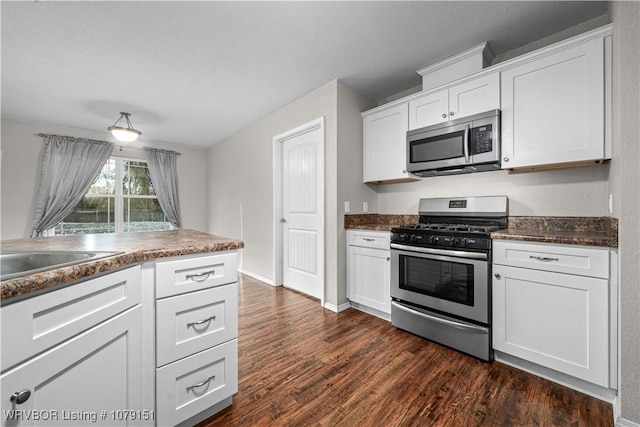 kitchen with dark wood finished floors, stainless steel appliances, dark countertops, white cabinets, and baseboards