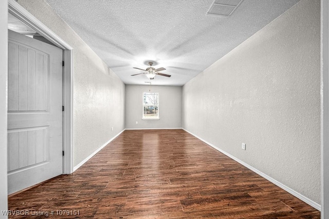 empty room featuring dark wood-style floors, visible vents, a textured wall, ceiling fan, and a textured ceiling