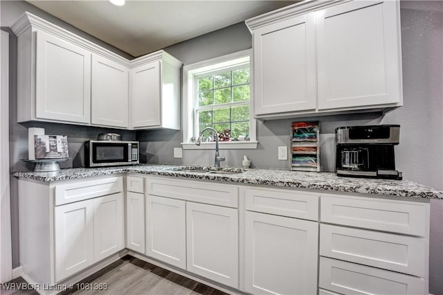 614 12th St, Van Buren, AR 72956 - kitchen featuring stainless steel microwave, a sink, white cabinets, light wood-style floors, and light stone counters