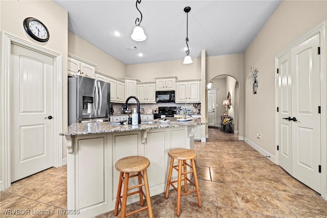 kitchen with a breakfast bar area, light stone counters, decorative backsplash, arched walkways, and black appliances