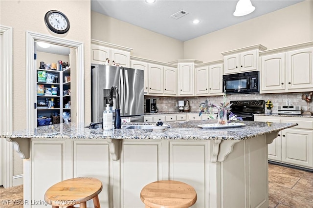 kitchen featuring light stone counters, visible vents, black appliances, a kitchen bar, and tasteful backsplash