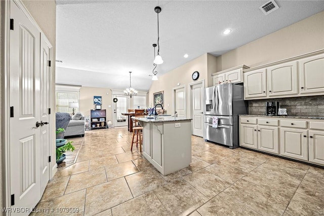 kitchen with visible vents, stainless steel fridge with ice dispenser, open floor plan, a kitchen bar, and decorative backsplash