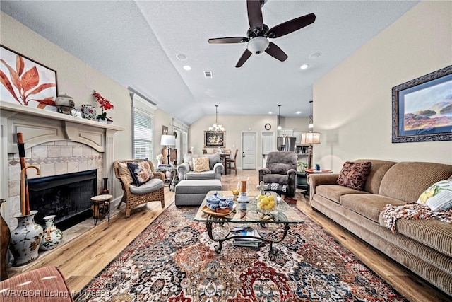 living room featuring visible vents, a tiled fireplace, vaulted ceiling, ceiling fan with notable chandelier, and wood finished floors