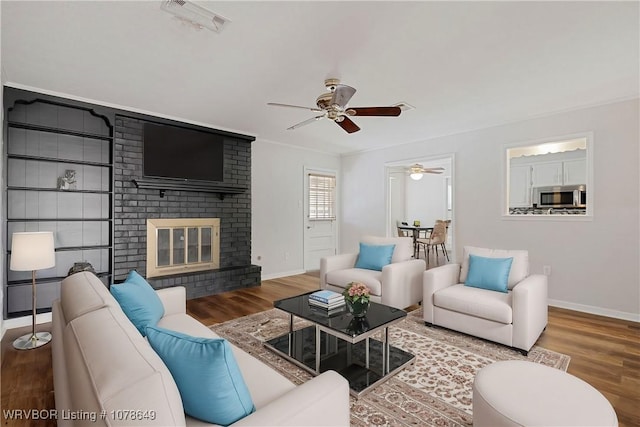 living room with a brick fireplace, crown molding, wood-type flooring, and ceiling fan