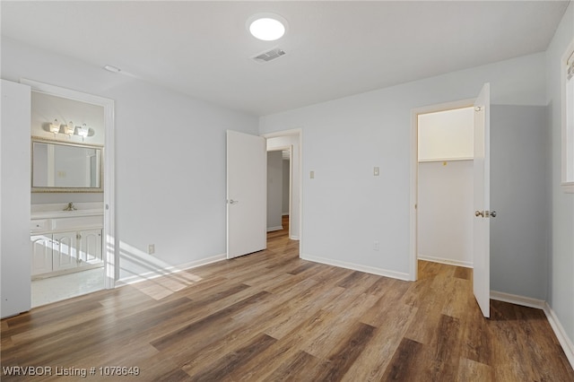 unfurnished bedroom featuring hardwood / wood-style flooring, a walk in closet, connected bathroom, and a closet