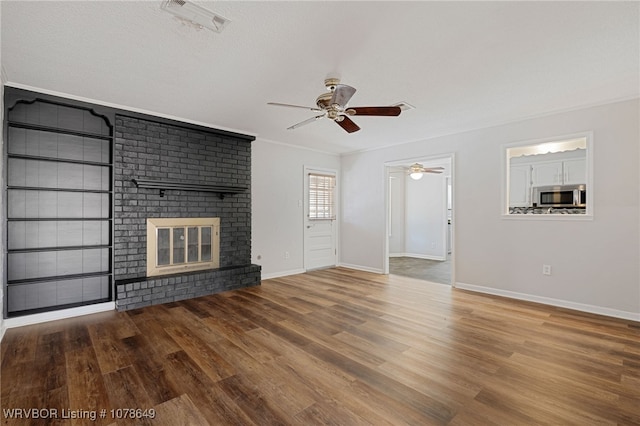 unfurnished living room featuring wood-type flooring, a brick fireplace, ceiling fan, and crown molding