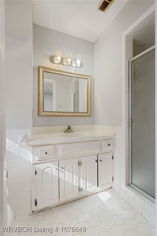 bathroom featuring vanity, a shower with door, a textured ceiling, and tile walls