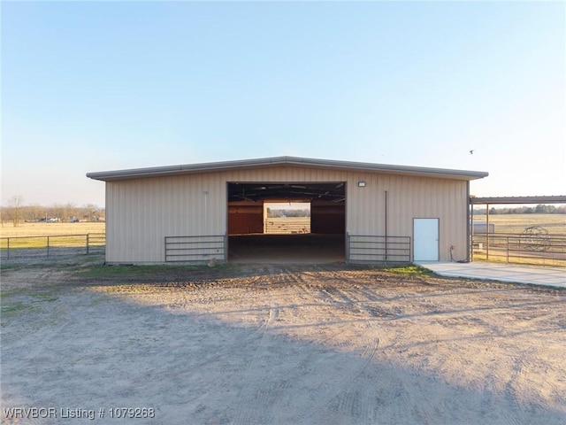 view of outdoor structure with a rural view, an outbuilding, driveway, and fence