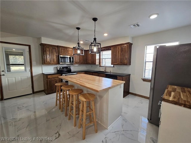 kitchen with a kitchen island, appliances with stainless steel finishes, a wealth of natural light, pendant lighting, and wooden counters