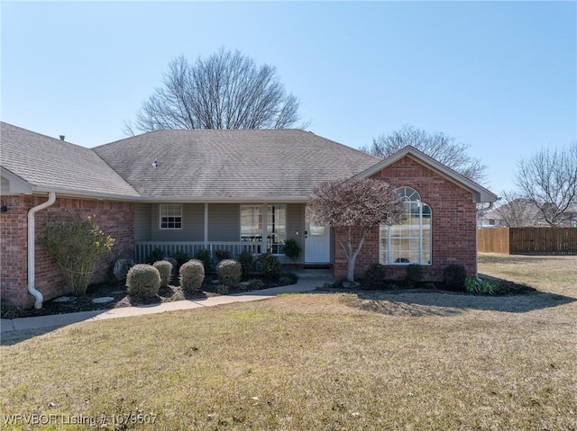 ranch-style home with a front lawn, fence, covered porch, and brick siding