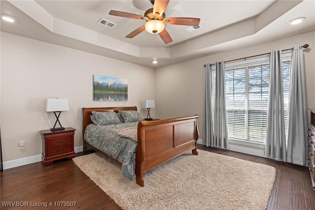 bedroom with visible vents, a raised ceiling, baseboards, and dark wood-style flooring