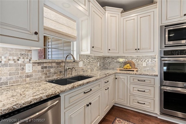 kitchen featuring a sink, light stone counters, backsplash, and appliances with stainless steel finishes