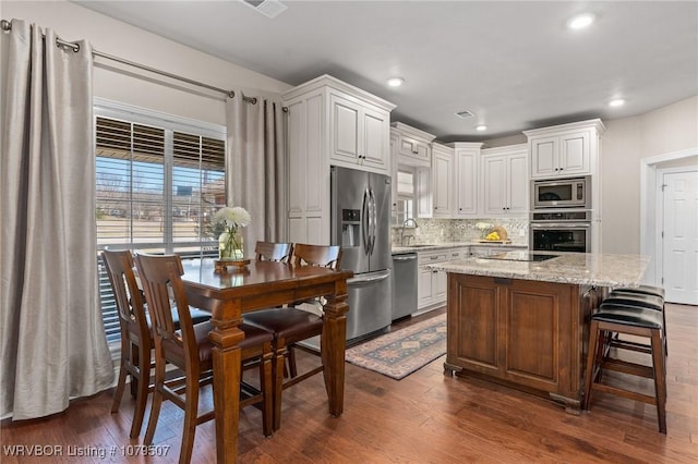 kitchen featuring dark wood-type flooring, tasteful backsplash, white cabinetry, stainless steel appliances, and light stone countertops