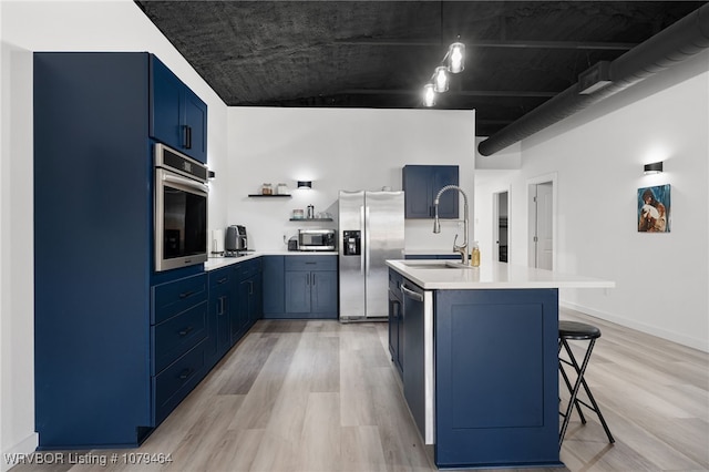 kitchen with blue cabinets, light wood-style flooring, appliances with stainless steel finishes, and a sink