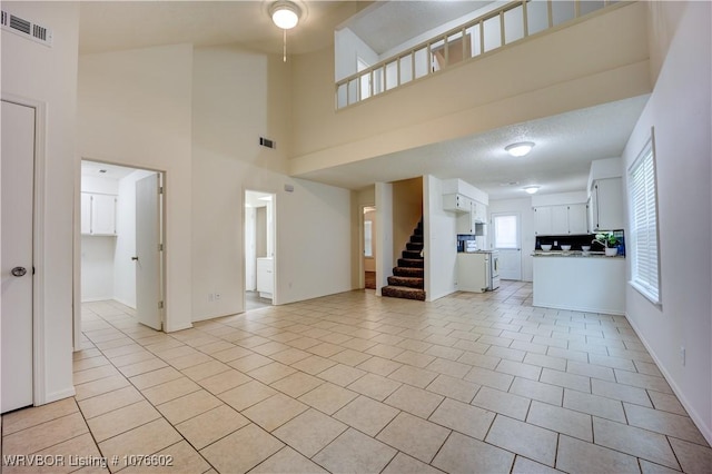 unfurnished living room featuring a textured ceiling, light tile patterned floors, and a high ceiling