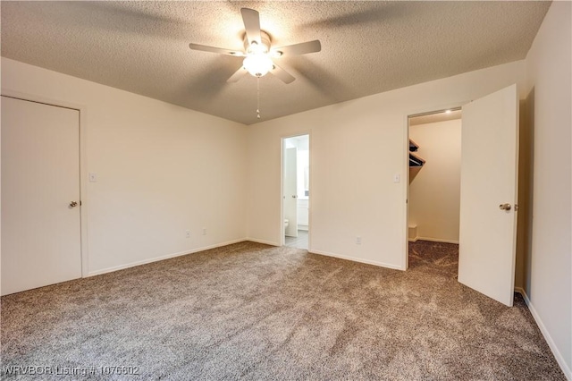 unfurnished bedroom with carpet flooring, a textured ceiling, a spacious closet, and ceiling fan