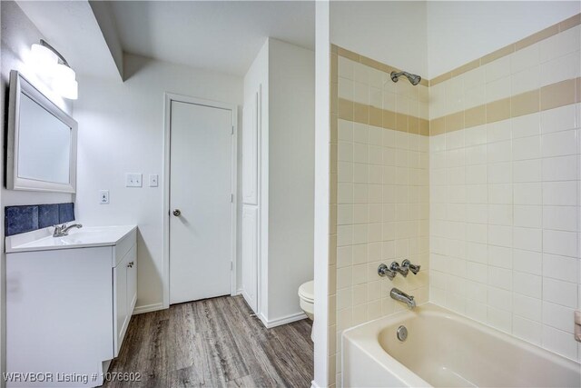 full bathroom featuring hardwood / wood-style flooring, vanity, tiled shower / bath combo, and toilet