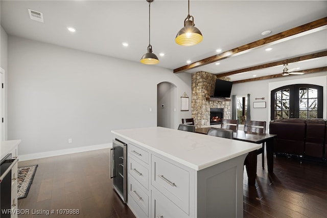 kitchen featuring wine cooler, a stone fireplace, visible vents, arched walkways, and dark wood-style flooring