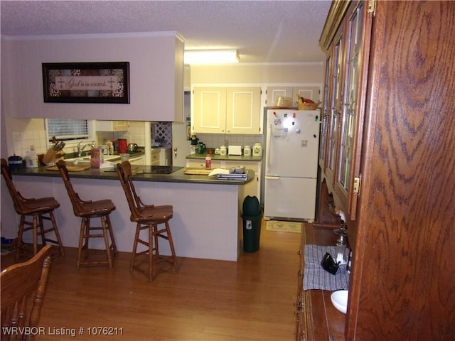 kitchen featuring white cabinetry, a kitchen breakfast bar, kitchen peninsula, white fridge, and hardwood / wood-style flooring