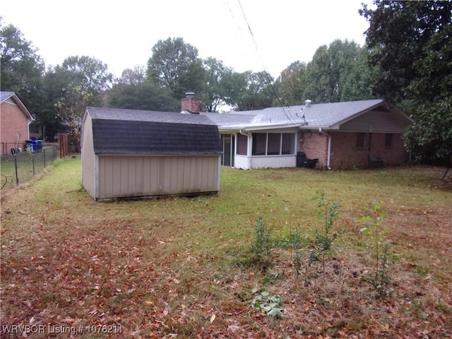 rear view of property featuring a sunroom, a yard, and a storage shed