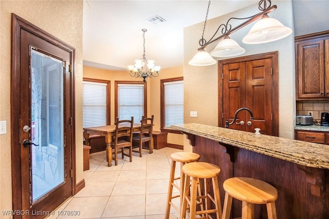 kitchen with light tile patterned flooring, light stone counters, hanging light fixtures, a kitchen breakfast bar, and decorative backsplash