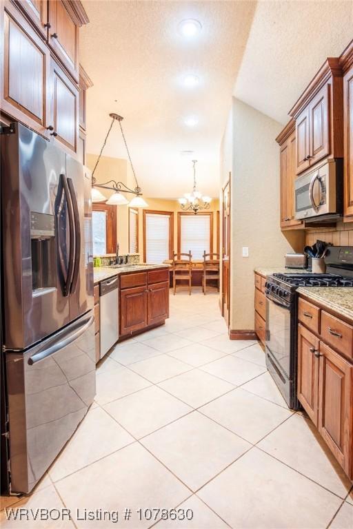 kitchen with pendant lighting, light tile patterned floors, lofted ceiling, appliances with stainless steel finishes, and a textured ceiling