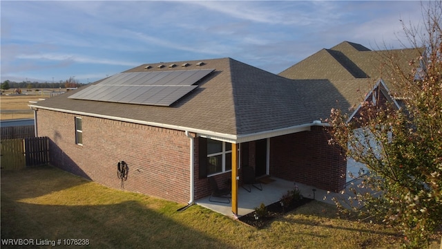 rear view of house with solar panels, a patio area, and a lawn