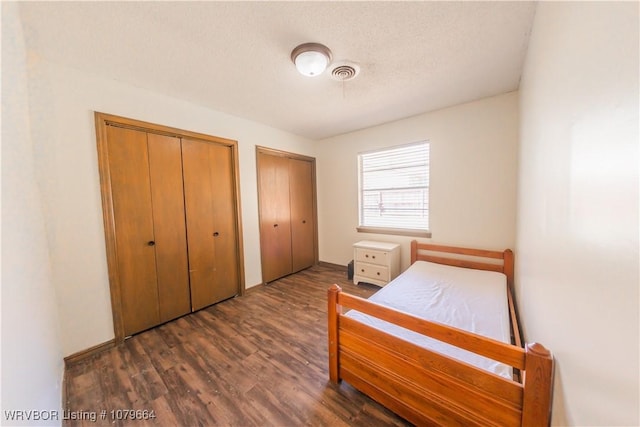 bedroom featuring visible vents, multiple closets, a textured ceiling, and wood finished floors