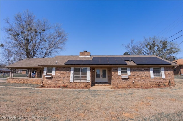 single story home with brick siding, solar panels, a chimney, and a front yard