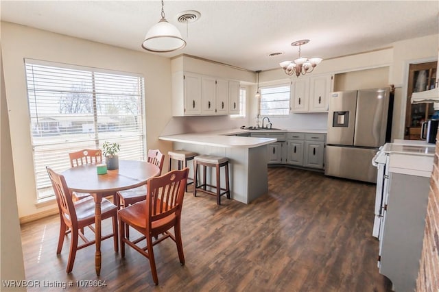 kitchen featuring visible vents, a peninsula, stainless steel fridge with ice dispenser, stove, and a chandelier