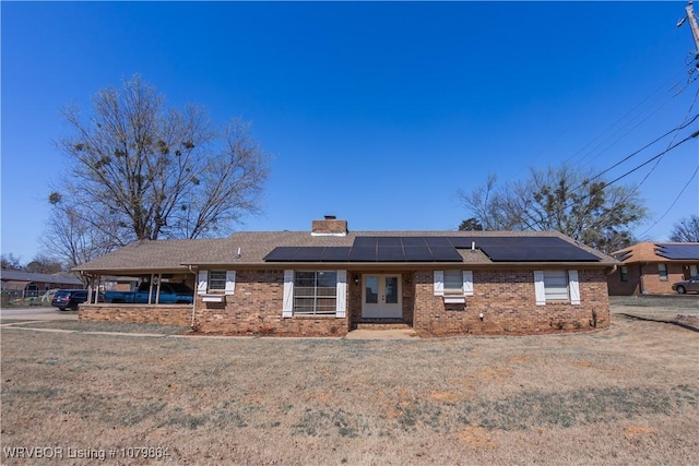 ranch-style home featuring brick siding, roof mounted solar panels, a chimney, and a front lawn