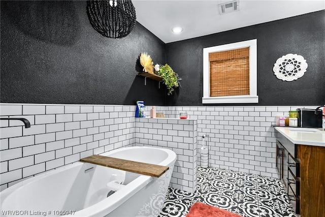 bathroom with tile patterned flooring, a washtub, tile walls, and vanity