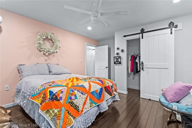 bedroom featuring a barn door, a closet, dark wood-type flooring, and ceiling fan