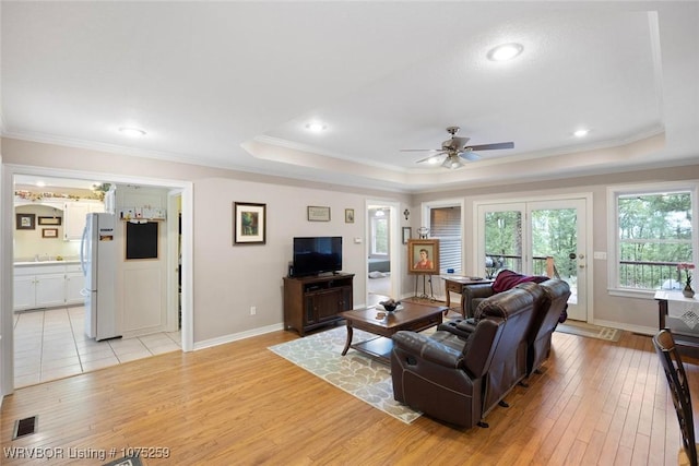 living room with a tray ceiling, ceiling fan, light hardwood / wood-style flooring, and ornamental molding