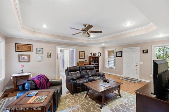 living room featuring a raised ceiling, crown molding, light hardwood / wood-style flooring, and ceiling fan