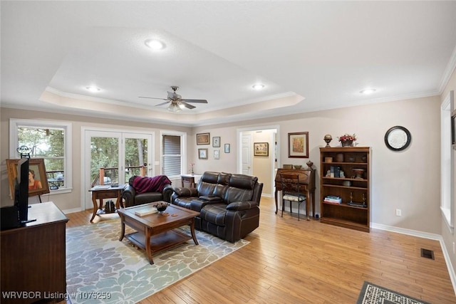 living room featuring a tray ceiling, ceiling fan, ornamental molding, and light wood-type flooring