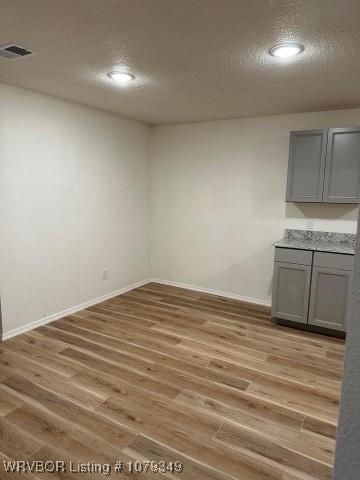 interior space featuring a textured ceiling, baseboards, visible vents, and light wood-style floors