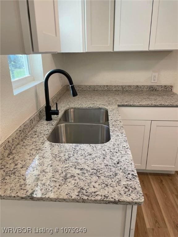 kitchen with light wood-type flooring, white cabinetry, a sink, and light stone countertops