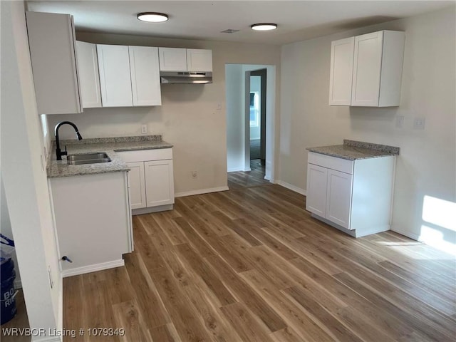 kitchen featuring light wood finished floors, light stone countertops, under cabinet range hood, white cabinetry, and a sink