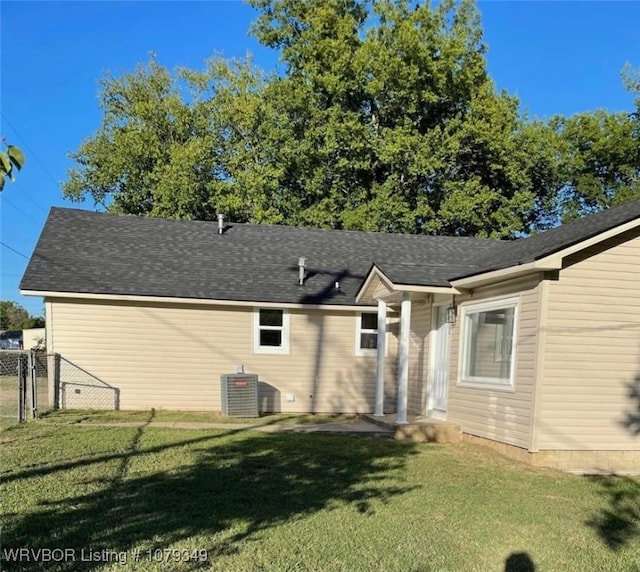 back of property featuring central AC unit, a shingled roof, fence, a yard, and a gate