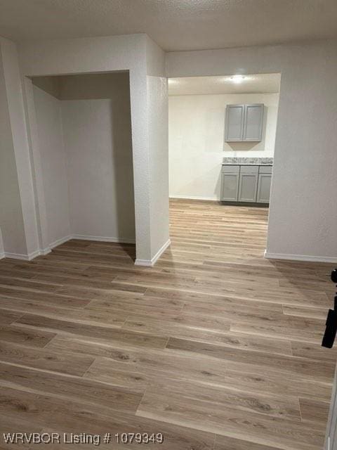 empty room featuring light wood-style floors, baseboards, and a textured ceiling