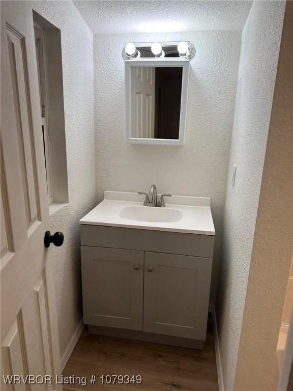 bathroom featuring a textured wall, wood finished floors, vanity, and baseboards