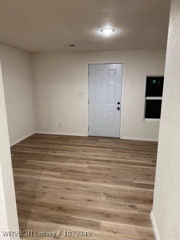 empty room featuring light wood-style flooring, baseboards, and a textured ceiling