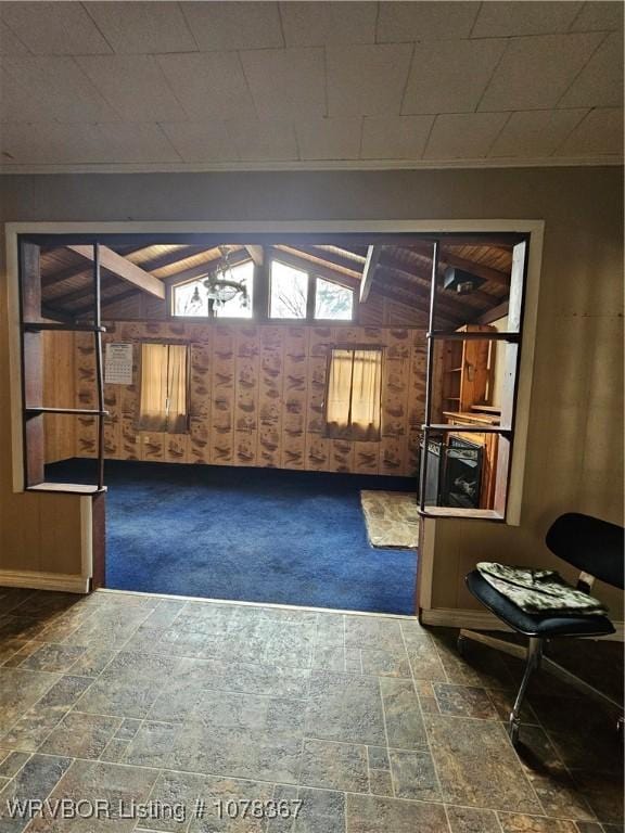 unfurnished room featuring lofted ceiling, dark carpet, and wood walls