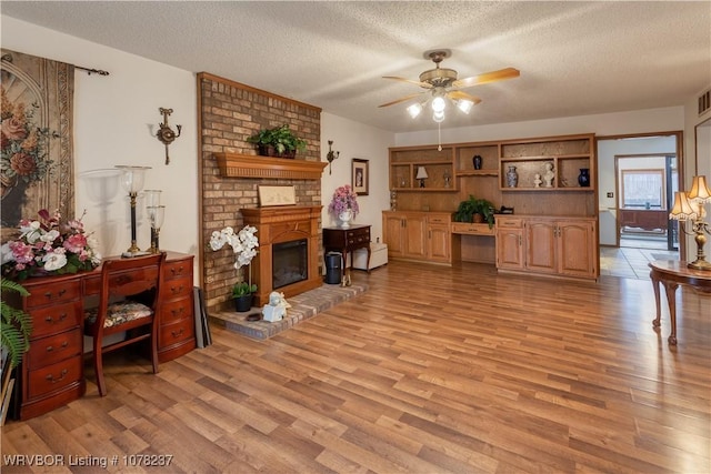 living room featuring a textured ceiling, ceiling fan, light wood-type flooring, and a fireplace