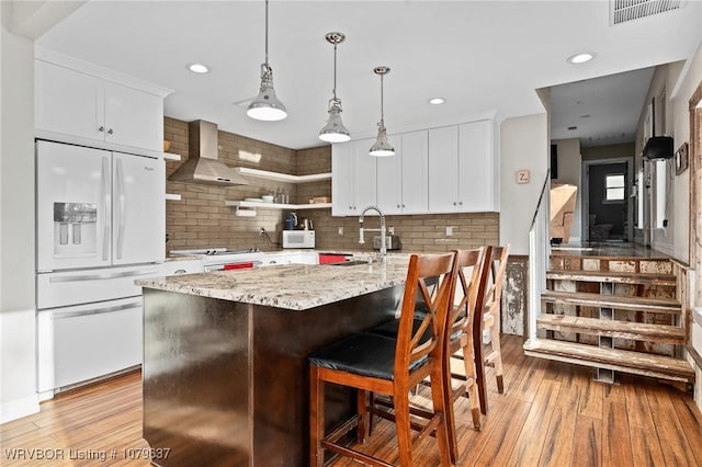 kitchen with wall chimney range hood, light wood-style flooring, white appliances, white cabinetry, and a sink