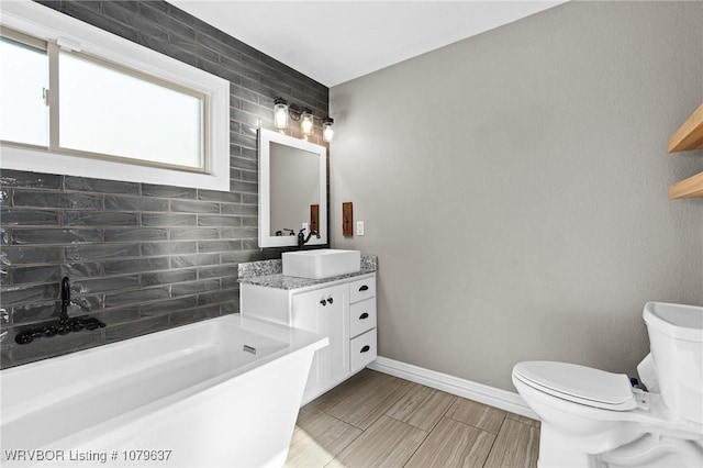 bathroom featuring baseboards, wood tiled floor, toilet, a bath, and vanity