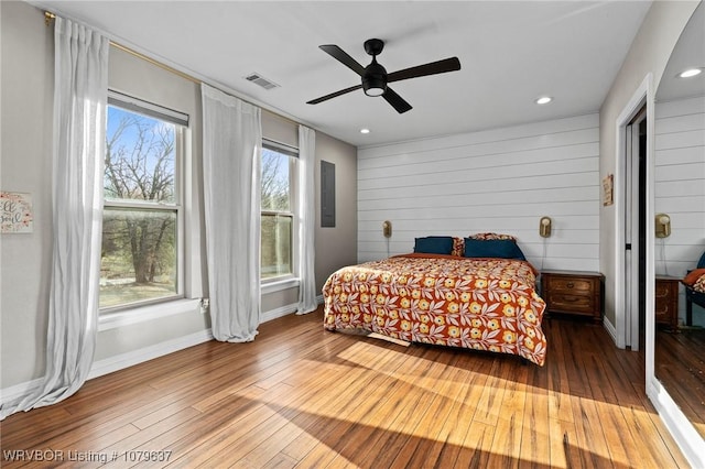 bedroom featuring wooden walls, visible vents, baseboards, hardwood / wood-style flooring, and a ceiling fan