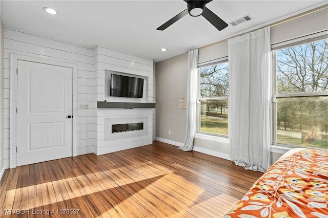 unfurnished living room featuring a glass covered fireplace, plenty of natural light, visible vents, and hardwood / wood-style floors