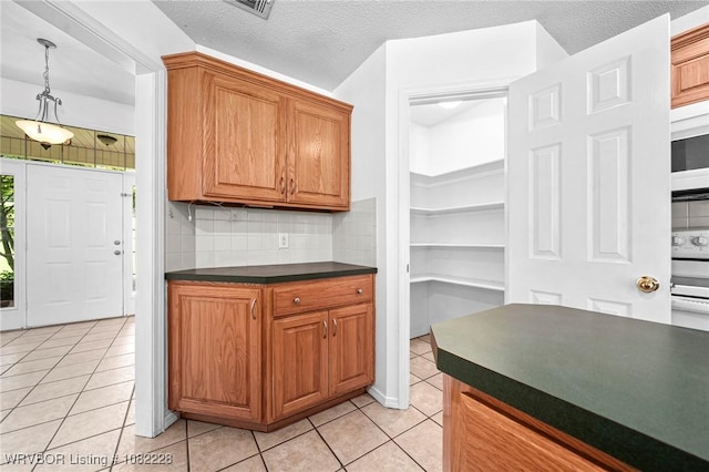 1121 Bourland St, Arkoma, OK 74901 - kitchen with dark countertops, light tile patterned floors, backsplash, and brown cabinets